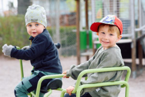 Två pojkar på förskolan är ute och leker på förskolans gård. De använder en grön taxicykel. Pojkarna tittar in i kamera och ler busigt
